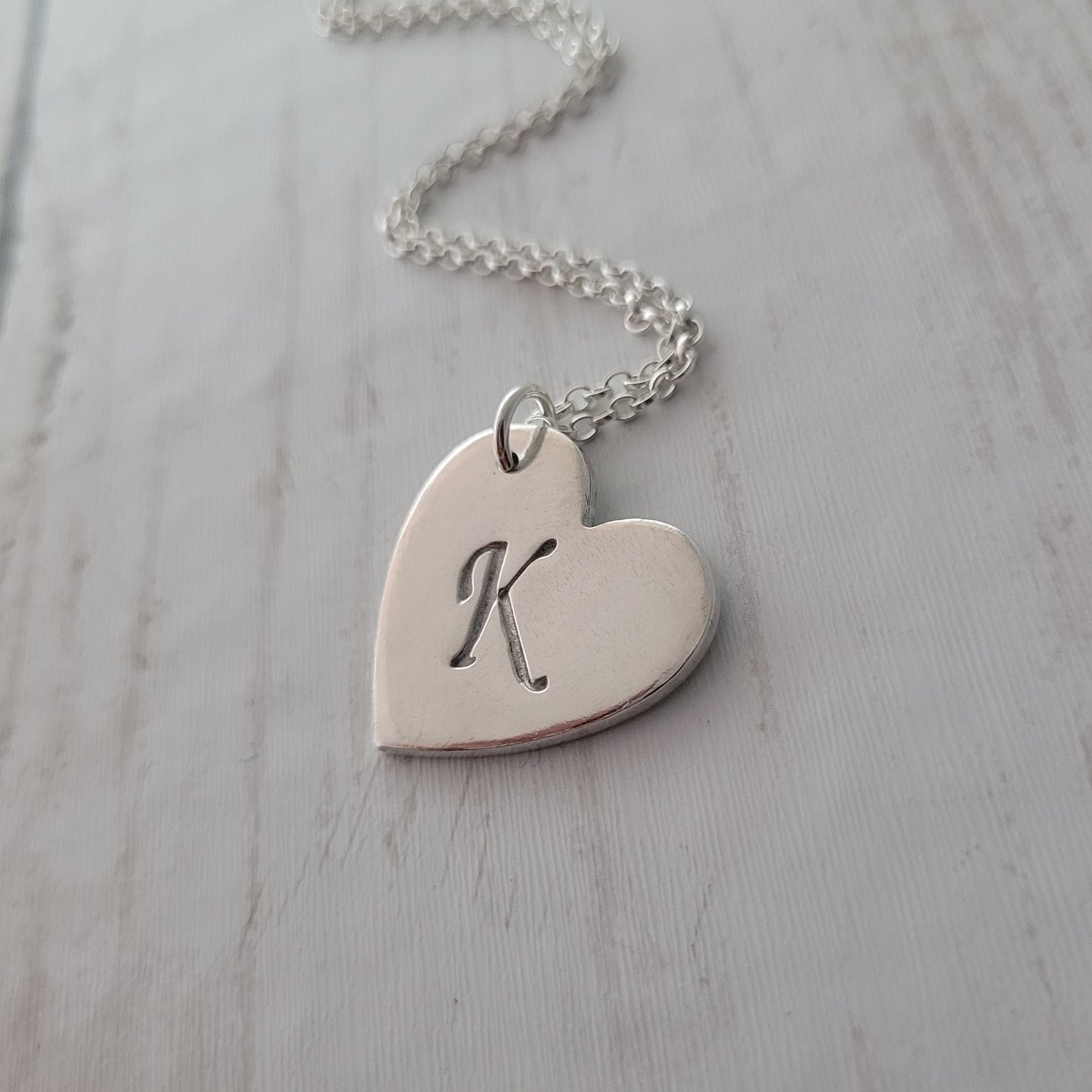 Heart-shaped silver pendant with a design on a light gray surface