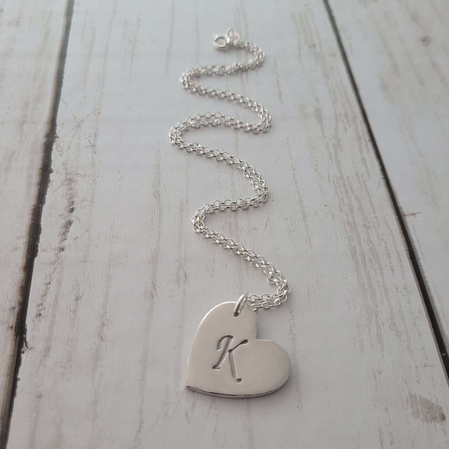 Silver heart-shaped pendant with engraved initials on a white wooden surface
