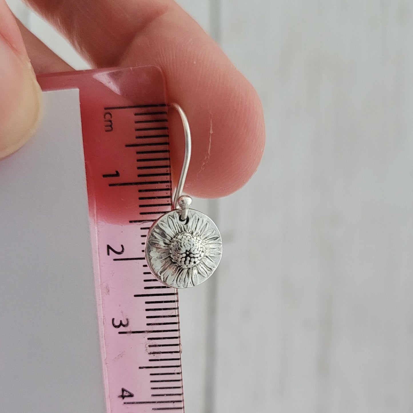 Silverflower earring being measured with a pink ruler against a light gray background