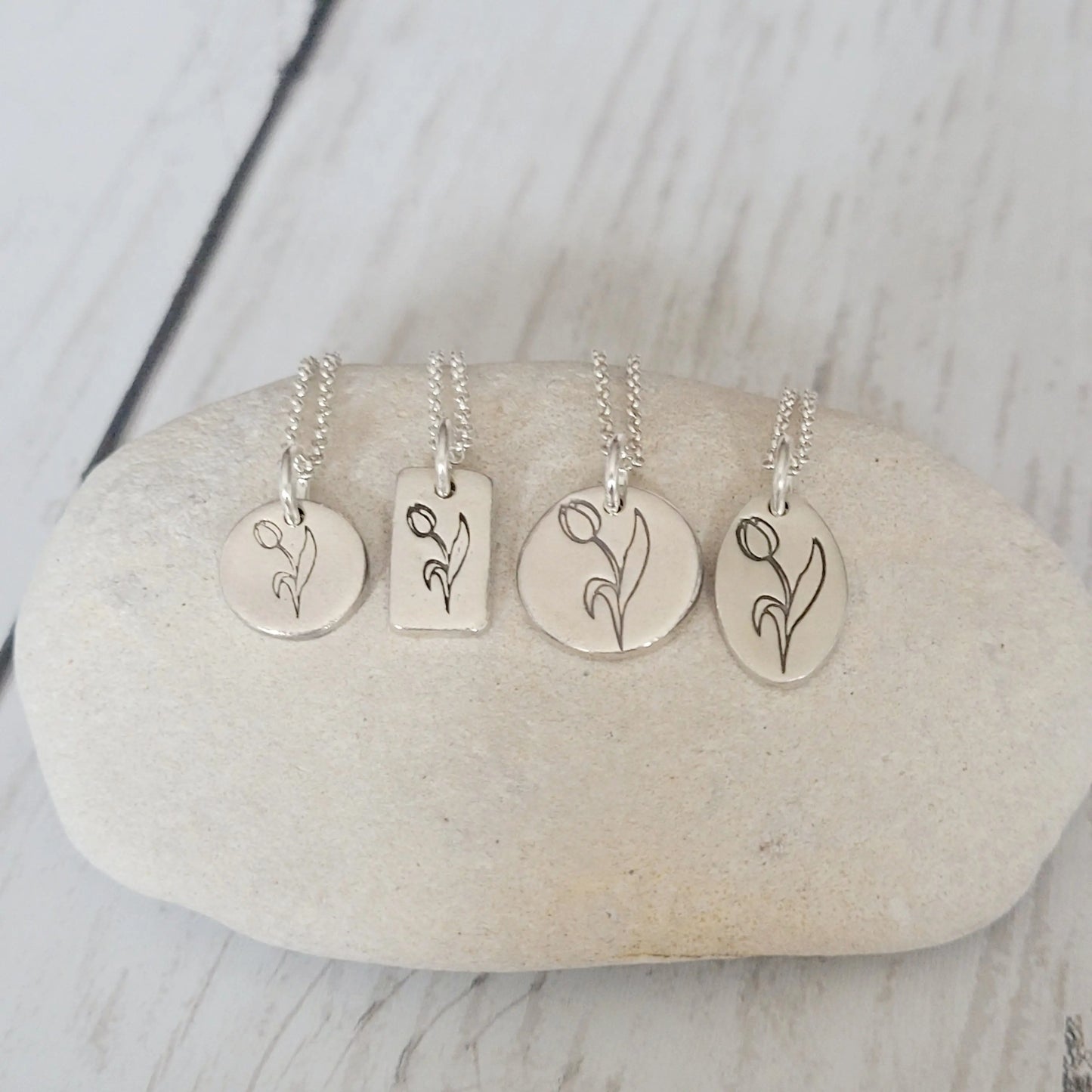 four silver necklaces with floral tulipb designs on a stone surface