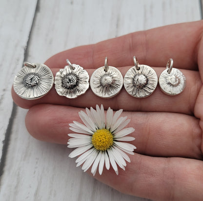 Five silver flower pendants on a hand next to a daisy flower.