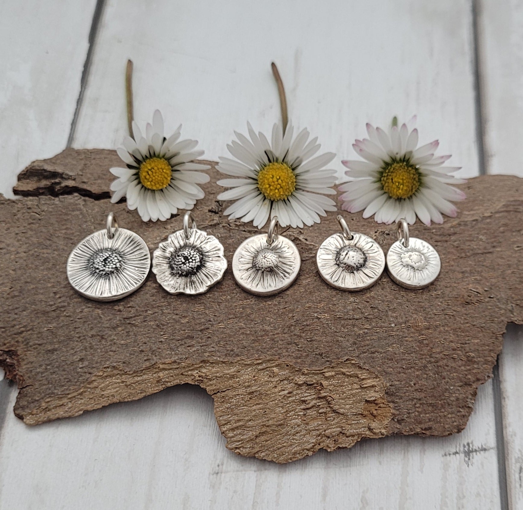 Silver botanical daisy flower pendants on a wooden surface with daisies