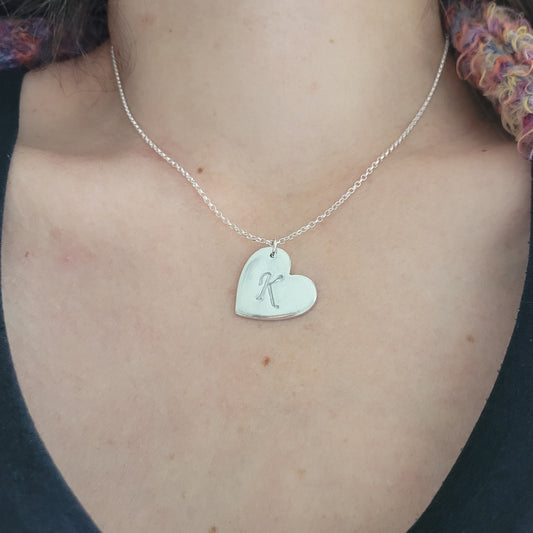 Sterling silver heart shaped pendant with engraved initial being worn