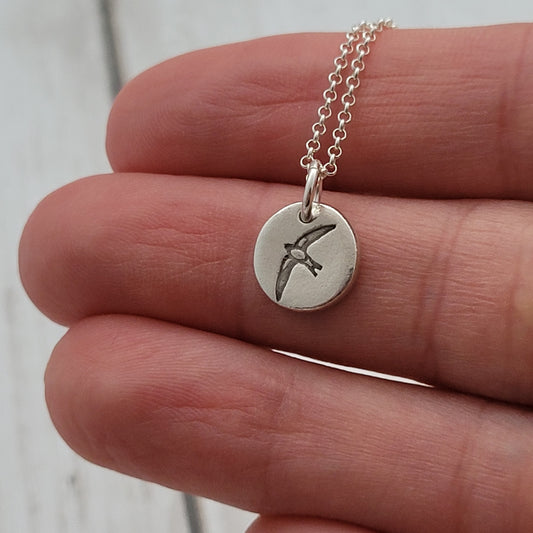 Sterling silver round bird necklace being held
