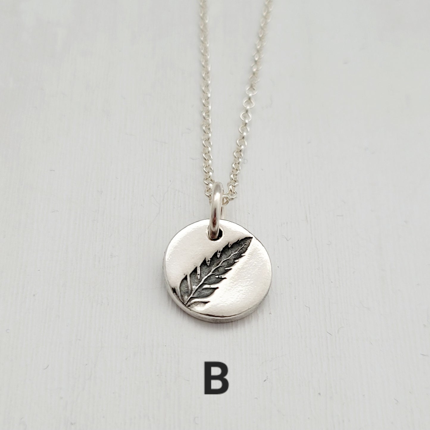 Silver necklace with a fern pendant on a light gray background