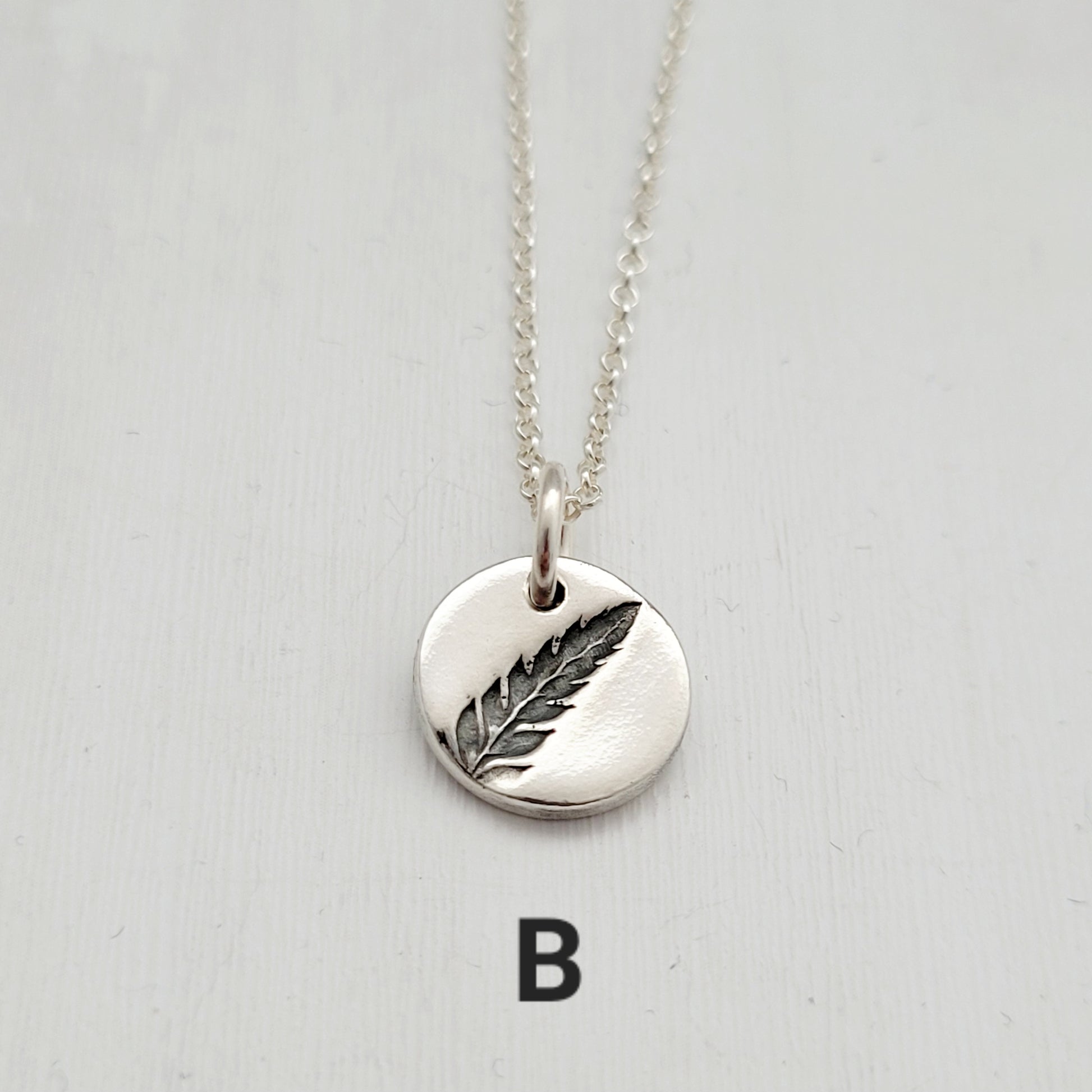 Silver necklace with a fern pendant on a light gray background
