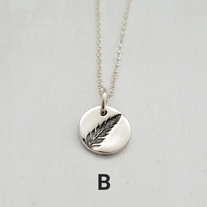 Silver necklace with a fern pendant on a light gray background