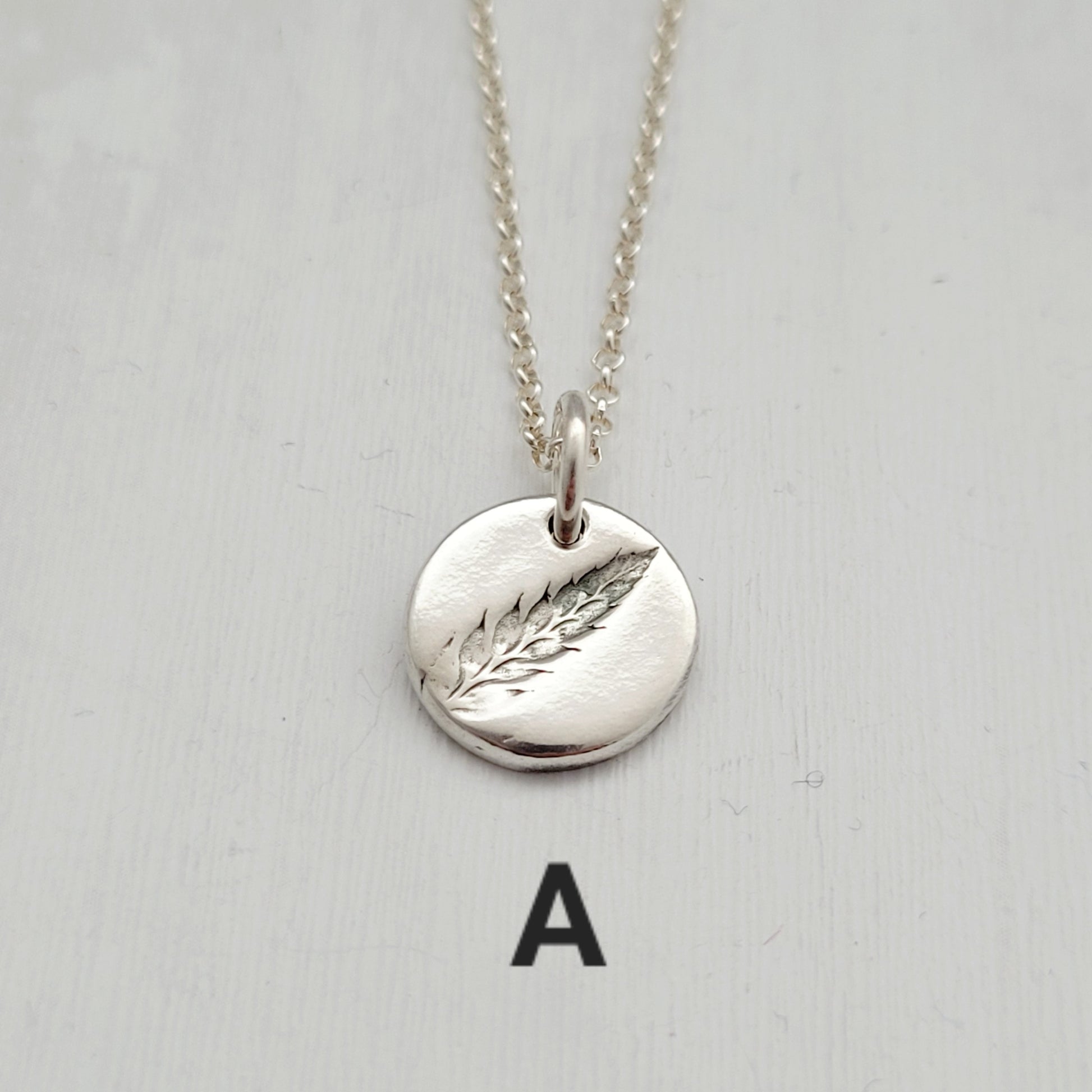 Silver necklace with a round pendant featuring a fern design on a light gray background.