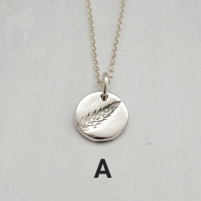 Silver necklace with a round pendant featuring a fern design on a light gray background.