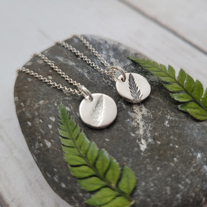 Silver necklaces with leaf pendants on a stone surface with green leaves.