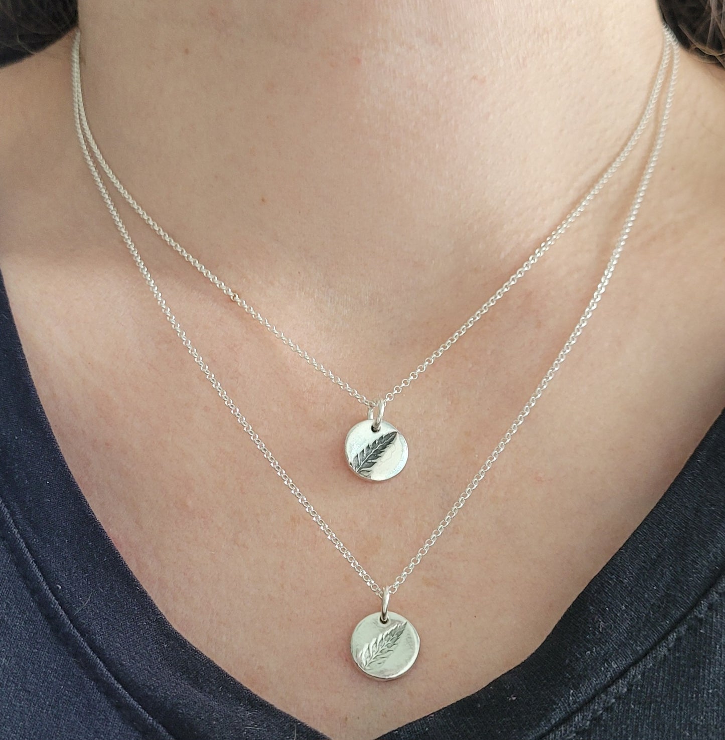 Silver necklaces with fern pendants on a person wearing a black top.