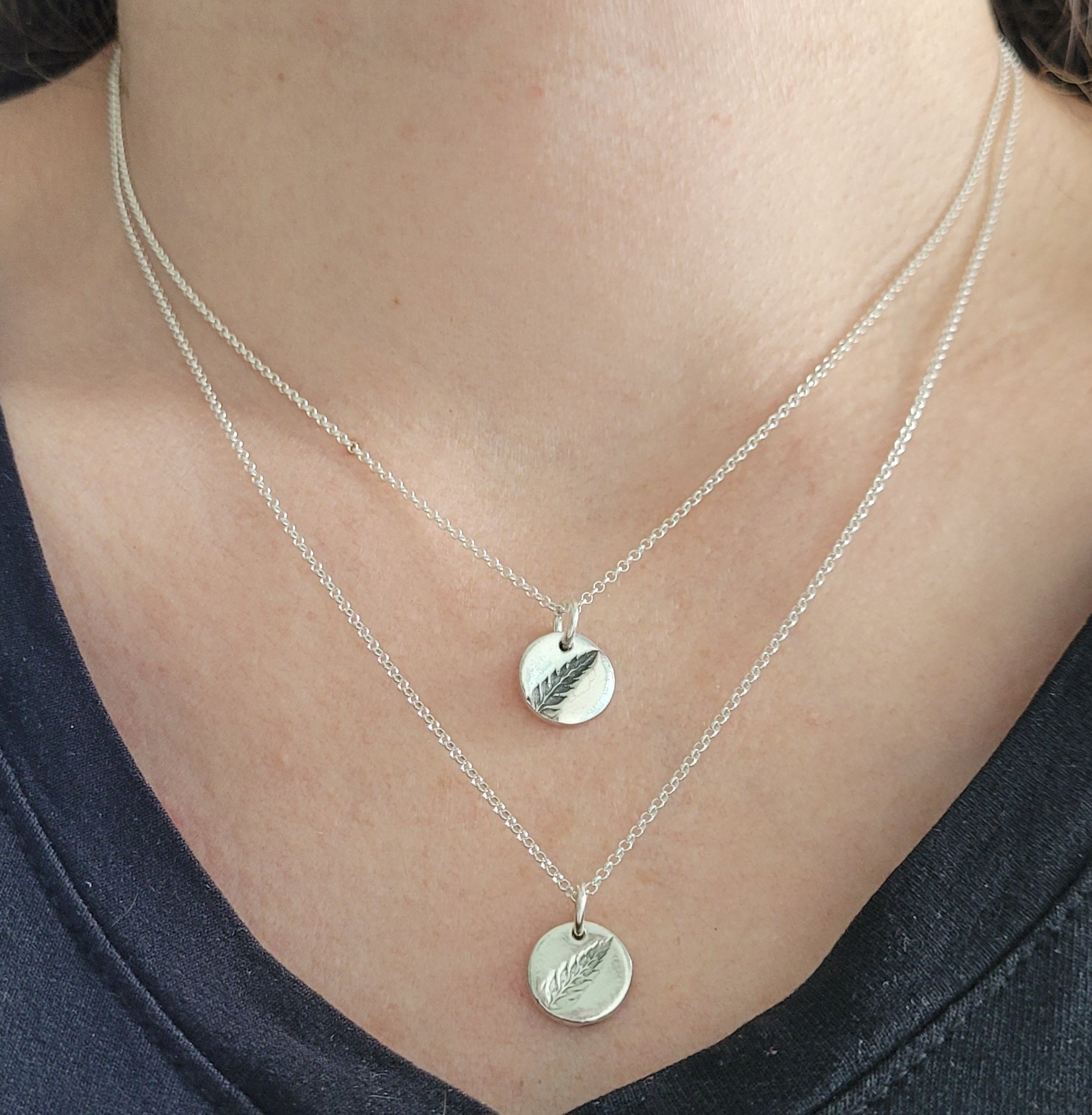 Silver necklaces with fern pendants on a person wearing a black top.