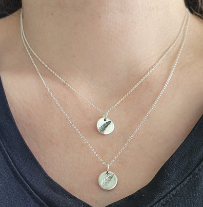 Silver necklaces with fern pendants on a person wearing a black top.