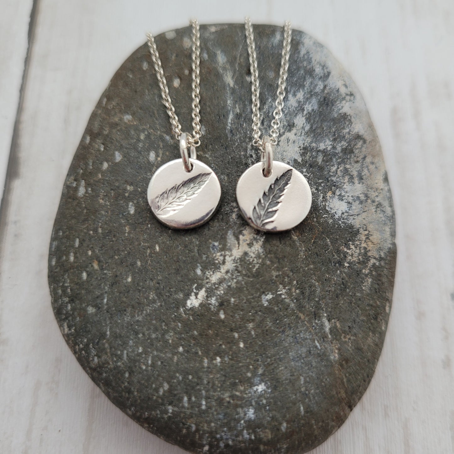 Two silver necklaces with leaf pendants on a stone surface