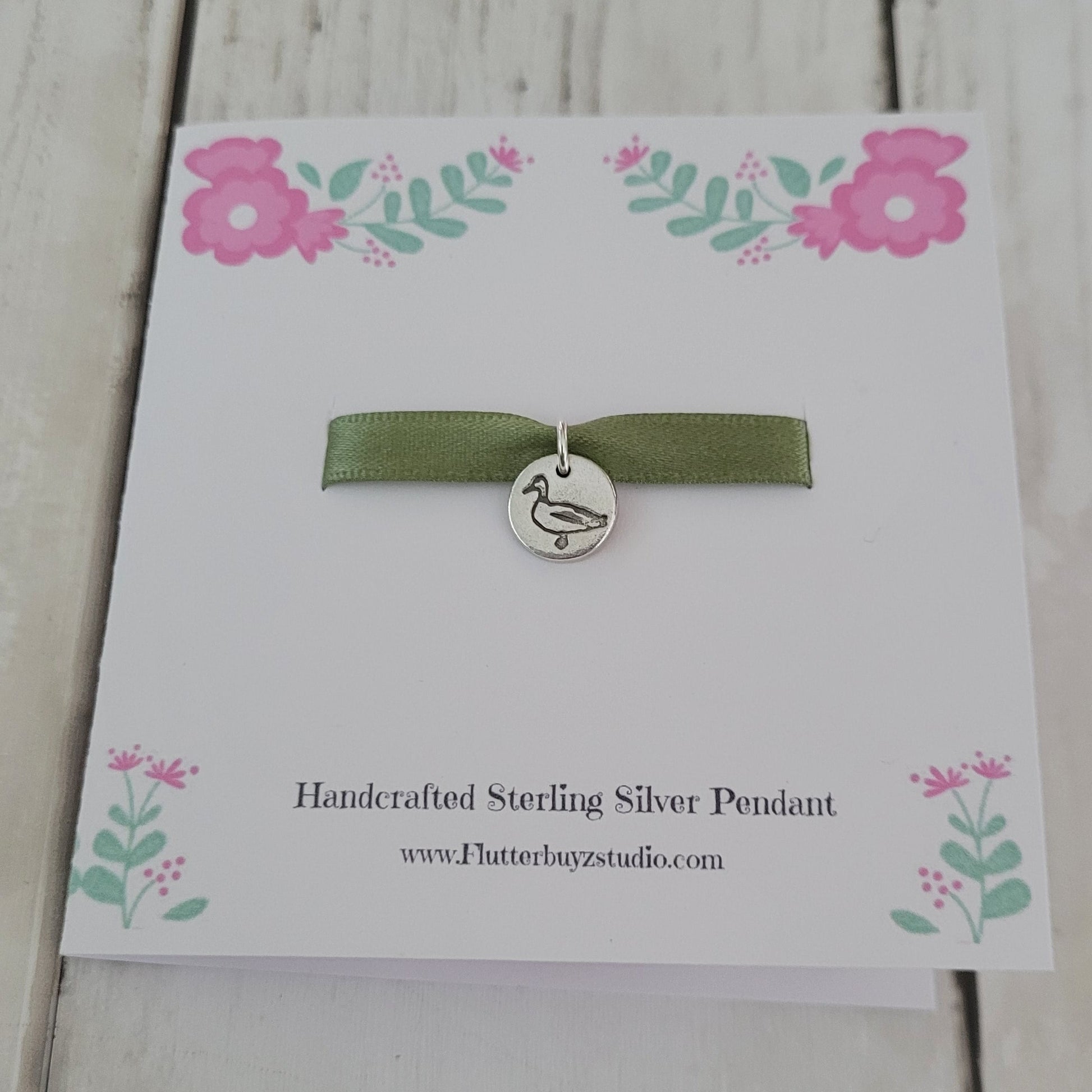 Silver duck bird pendant on a floral card with a white background