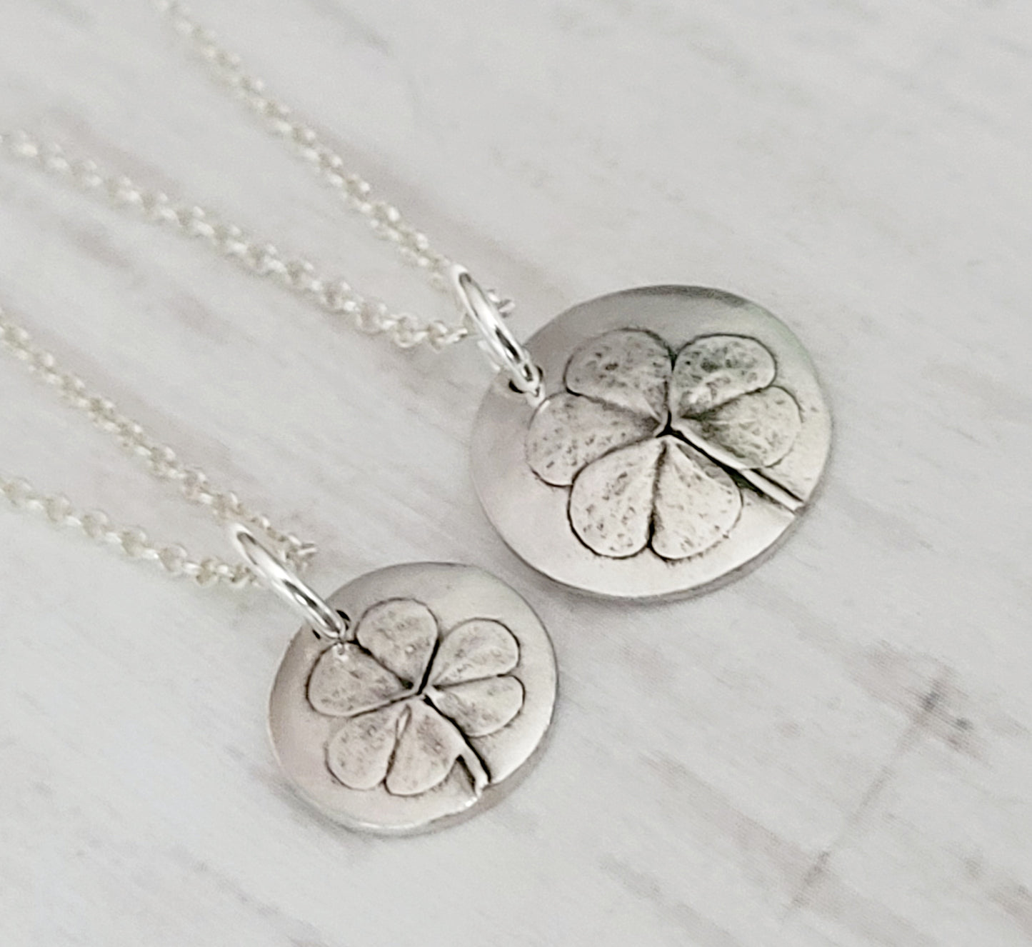 Two silver clover pendants on a surface