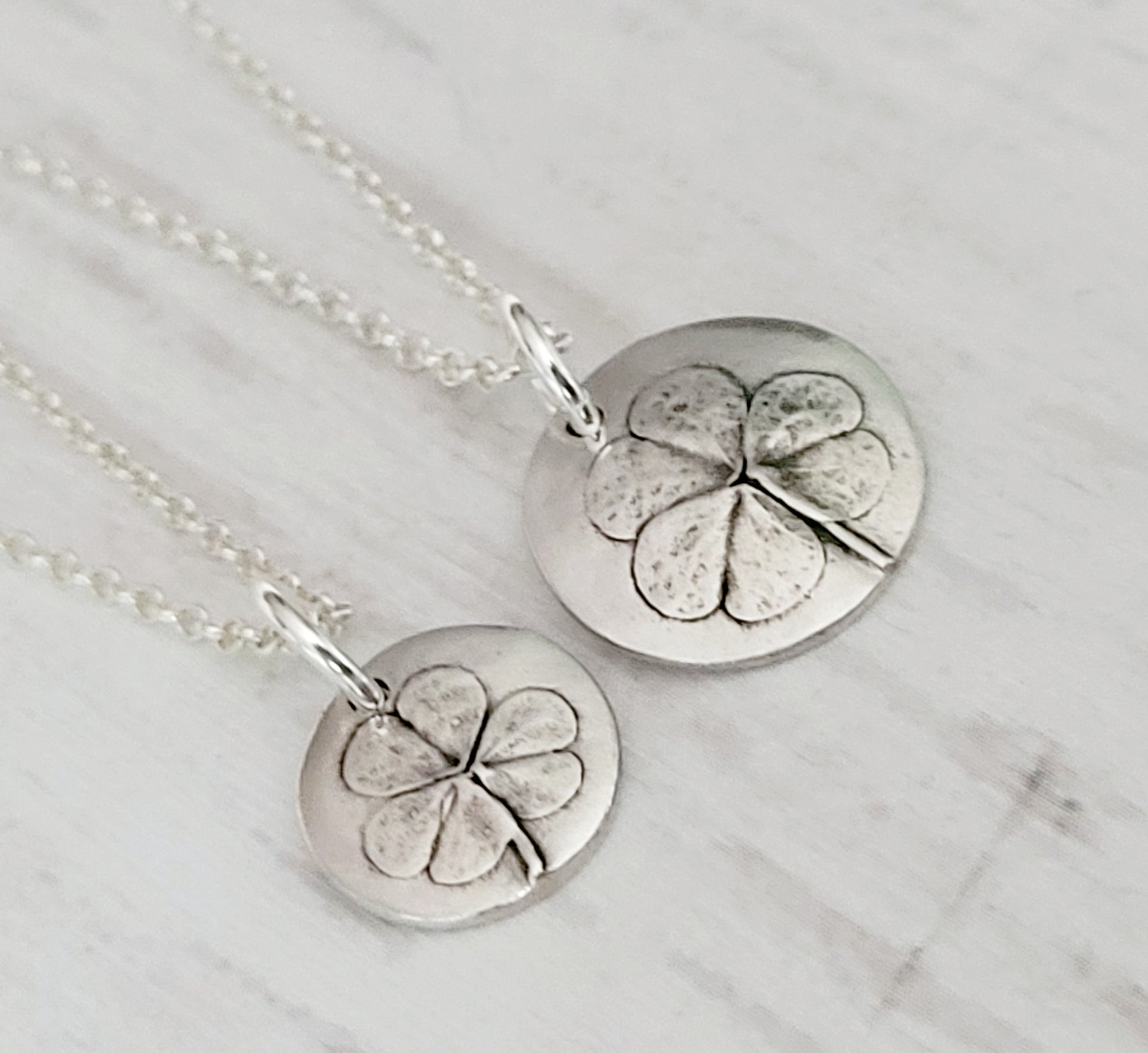 Two silver clover pendants on a surface