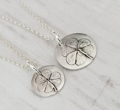 Two silver clover pendants on a surface