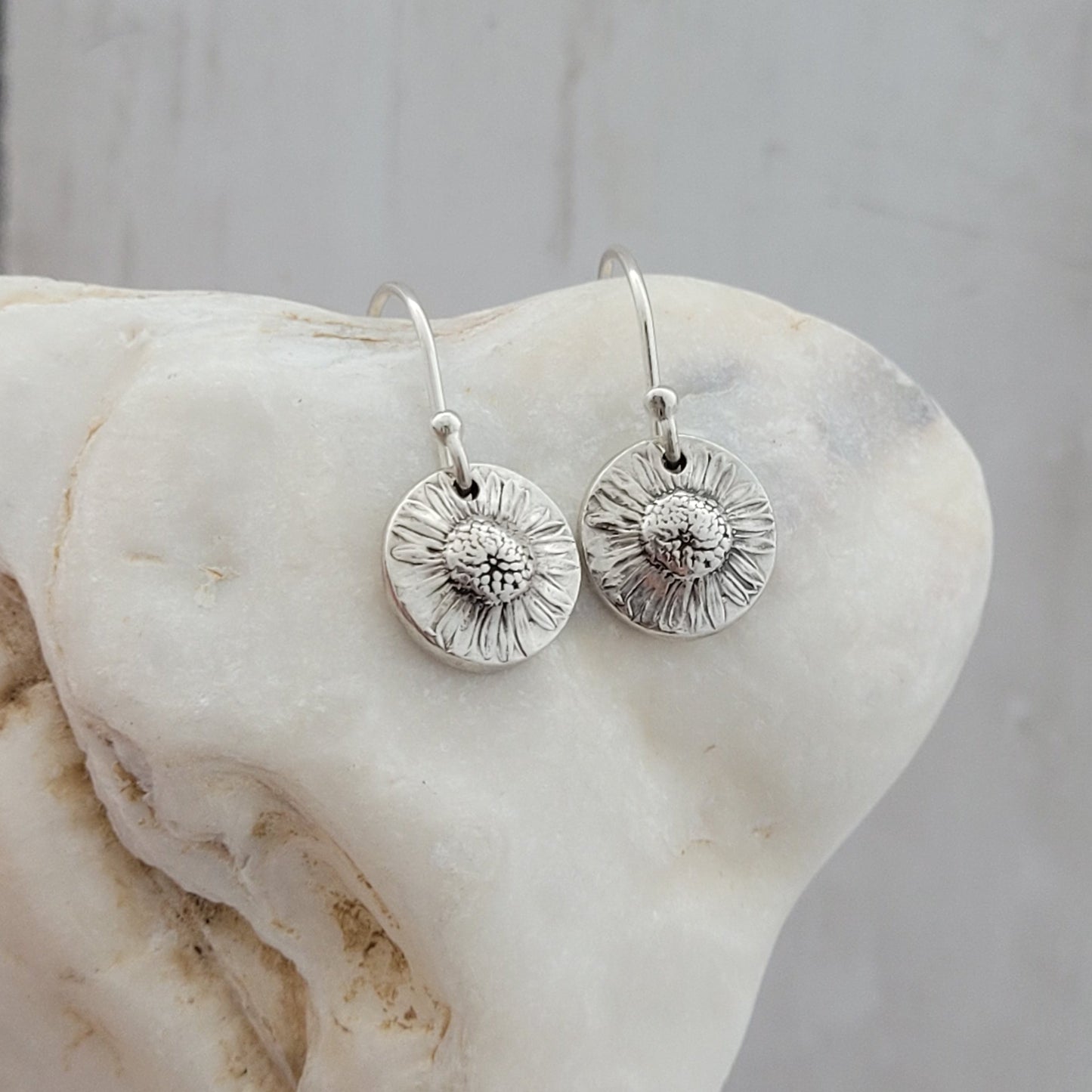 Silver floral earrings on a shell surface