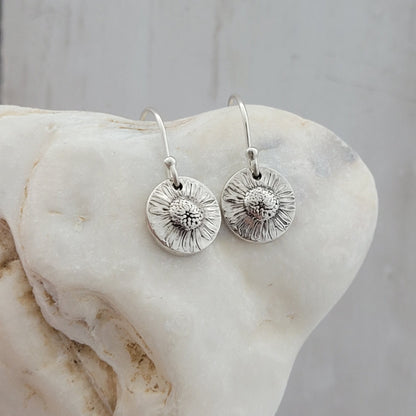 Silver floral earrings on a shell surface