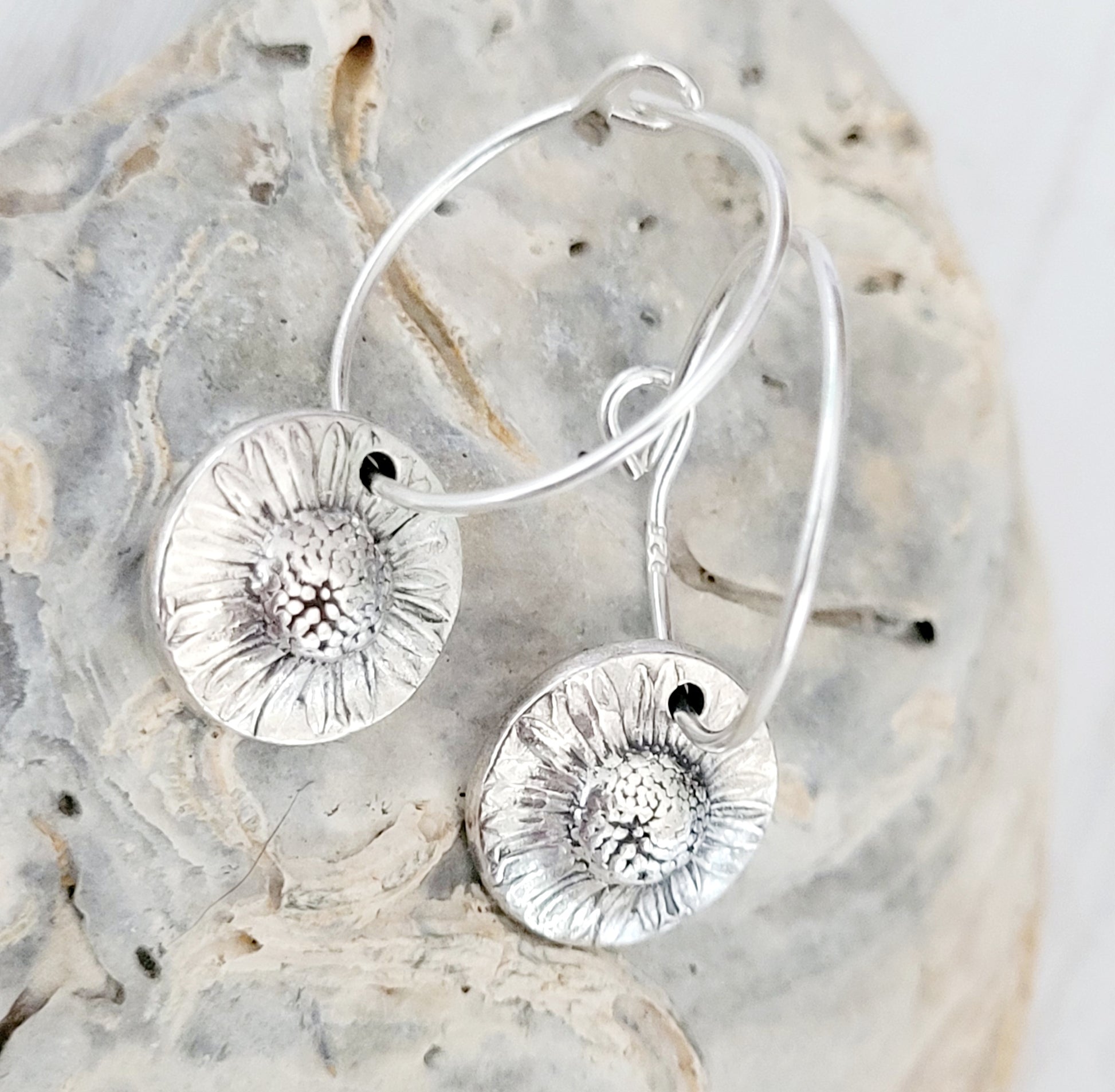 Silver floral hoop earrings on a textured stone surface