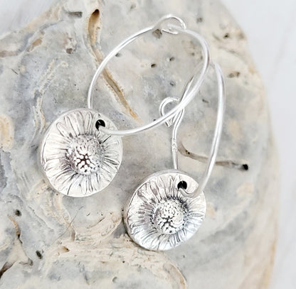 Silver floral hoop earrings on a textured stone surface