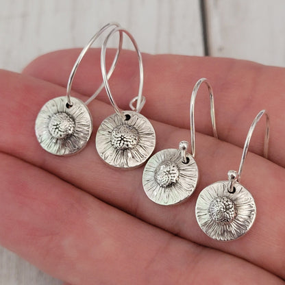 Silver floral earrings on a hand with a light wooden background