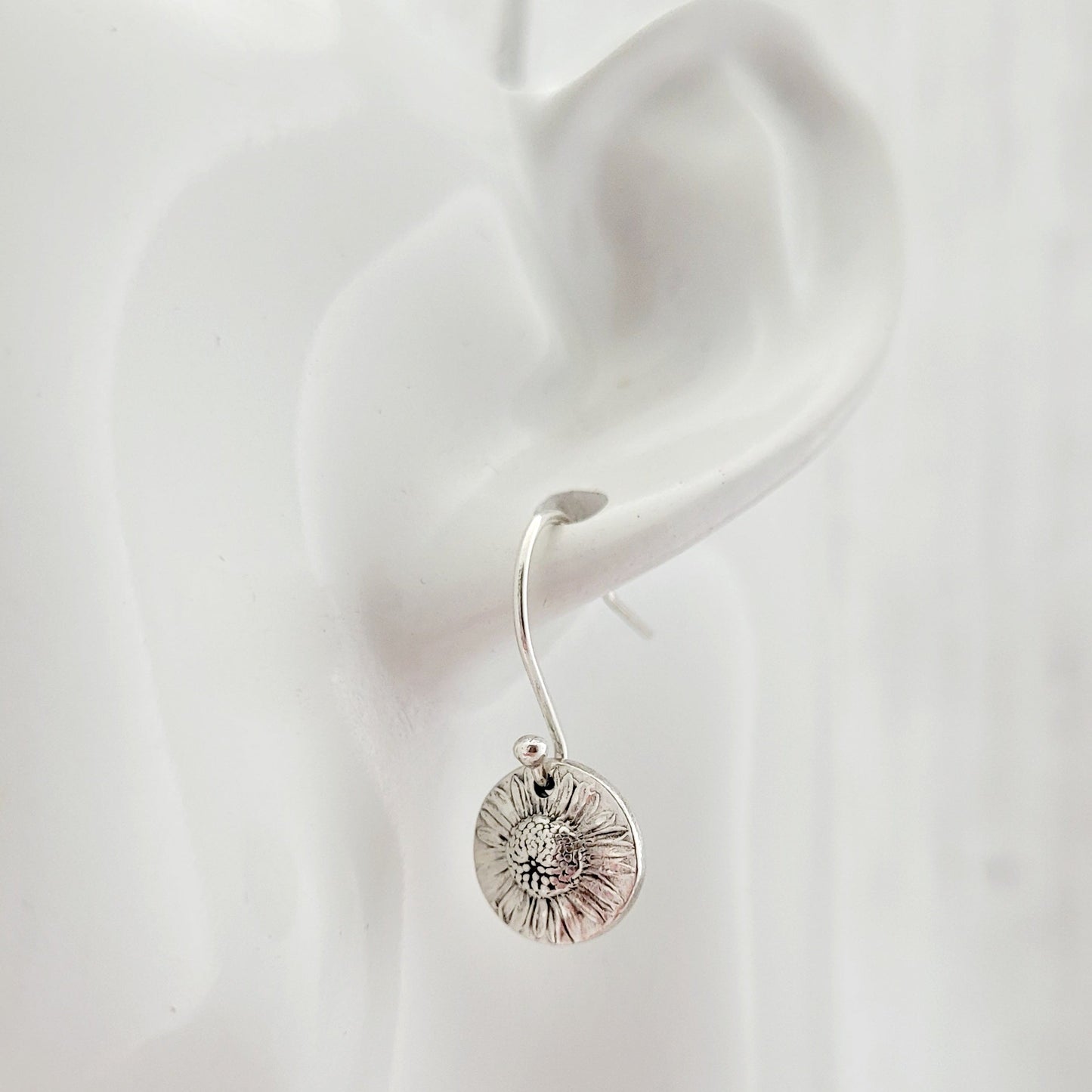 Silver daisy earring worn on a white ear with a plain background