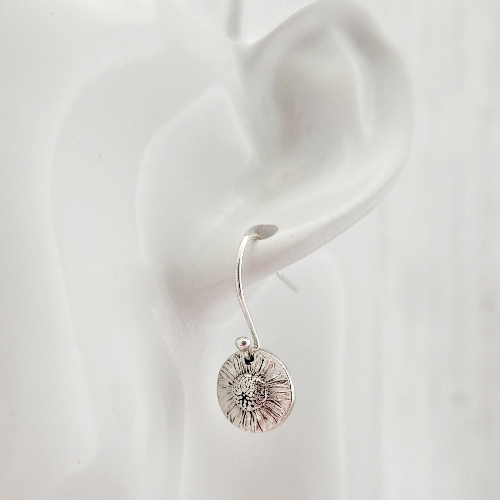 Silver daisy earring worn on a white ear with a plain background