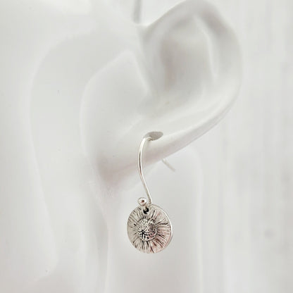 Silver daisy earring worn on a white ear with a plain background
