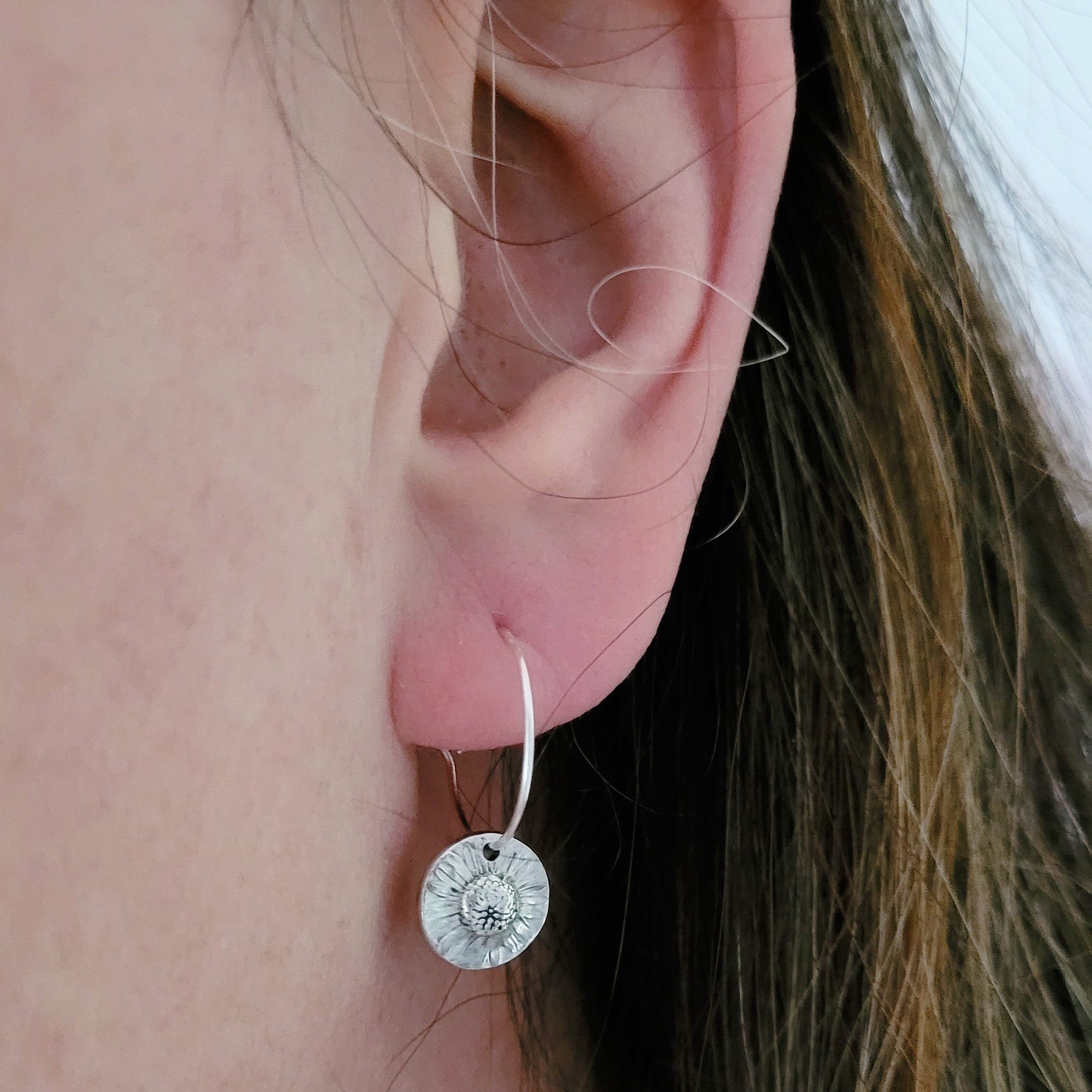 Close-up of an ear wearing a silver daisy hoop earring 