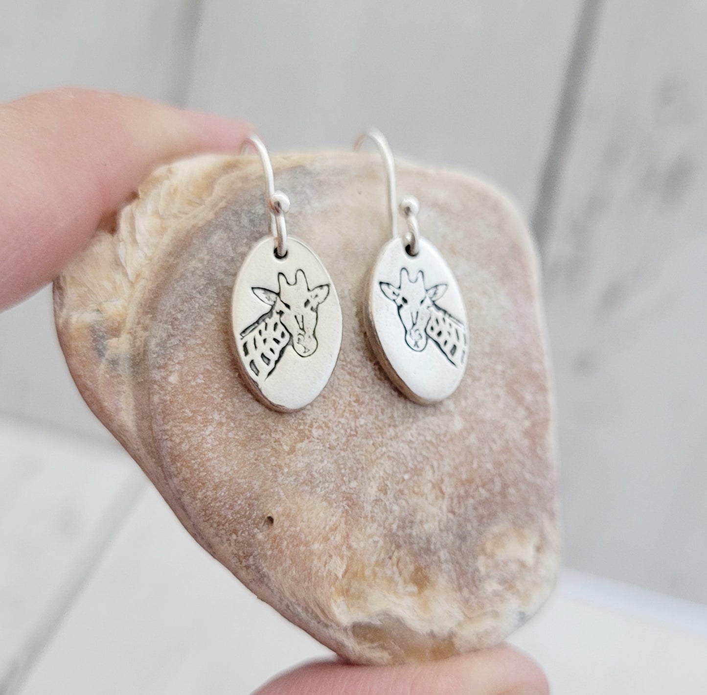 Silver earrings with giraffe designs on a stone surface