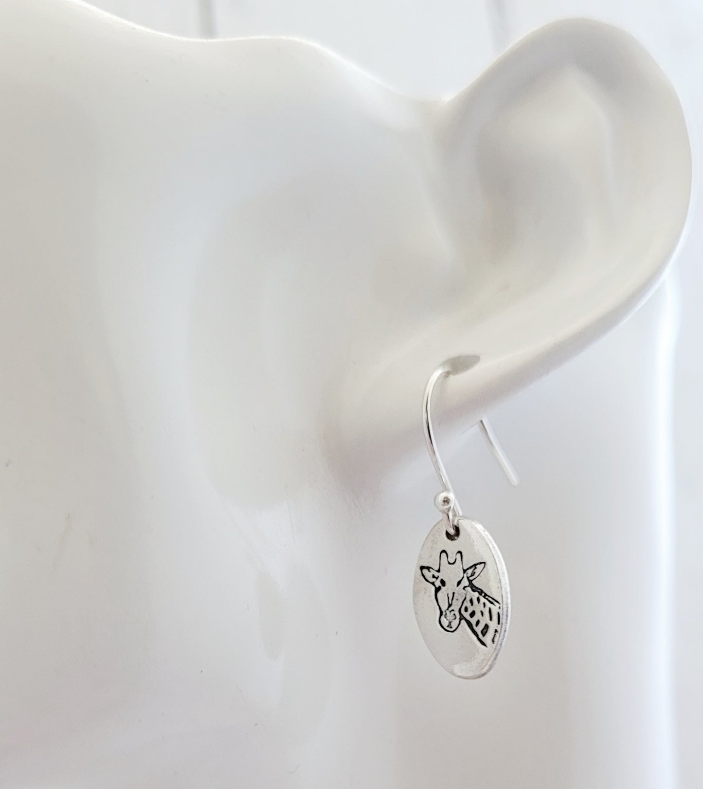 Silver earring with a giraffe design on an ear against a white background