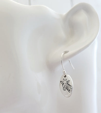 Silver earring with a giraffe design on an ear against a white background
