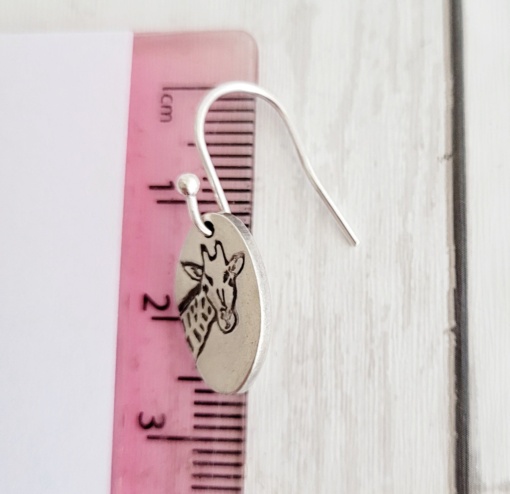 Silver earring with giraffe design on a pink ruler for scale