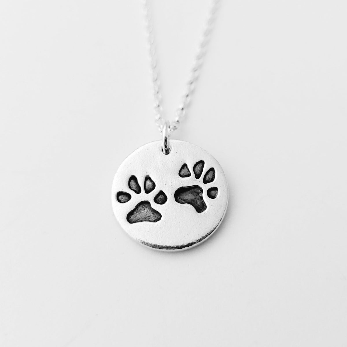 round pendant with two imprinted black paw prints