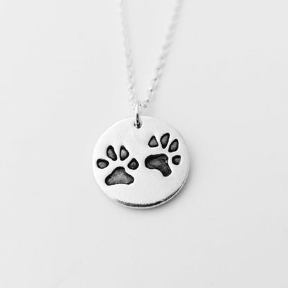 round pendant with two imprinted black paw prints