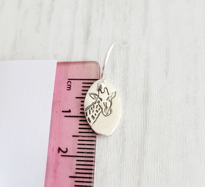 Silver charm with giraffe design on a pink ruler against a white background