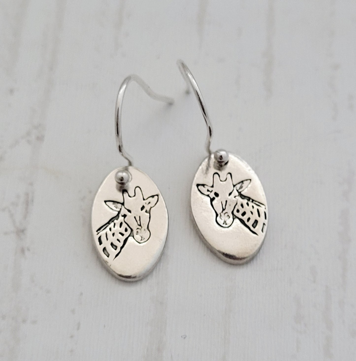 Silver earrings with giraffe designs on a light gray background