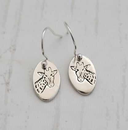 Silver earrings with giraffe designs on a light gray background