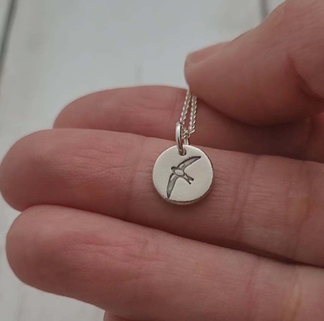 Sterling silver round swallow bird pendant shown on hand