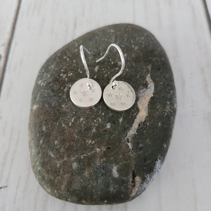 Silver round star earrings on a dark stone surface