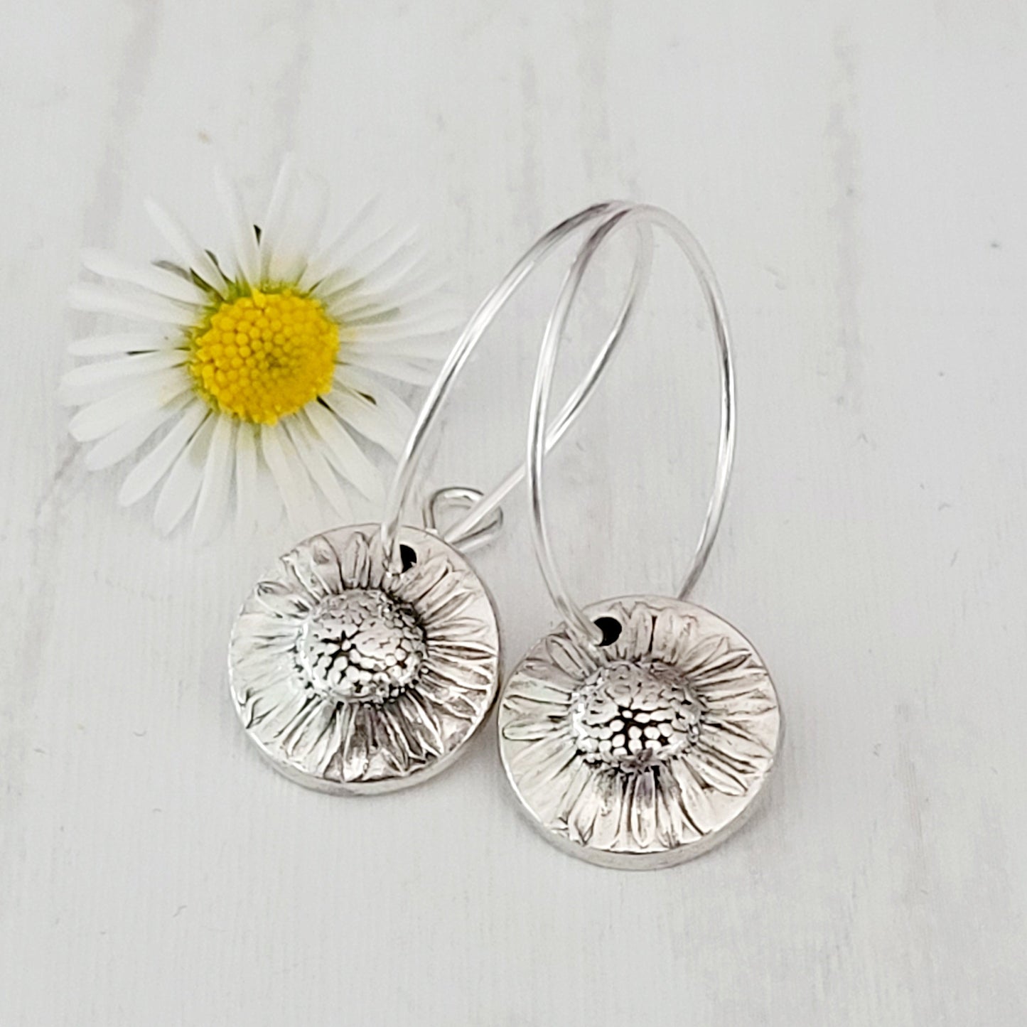 Silver floral earrings on a light gray background with a daisy flower.