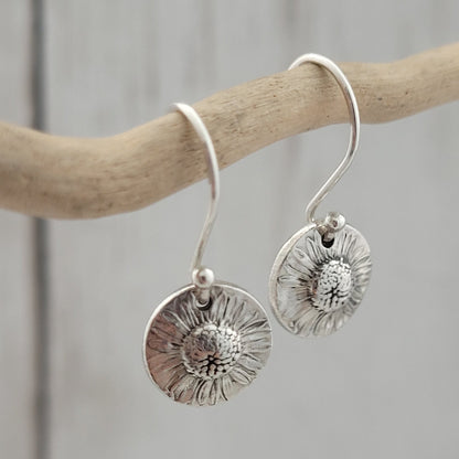 Silver floral earrings hanging from a branch on a neutral background