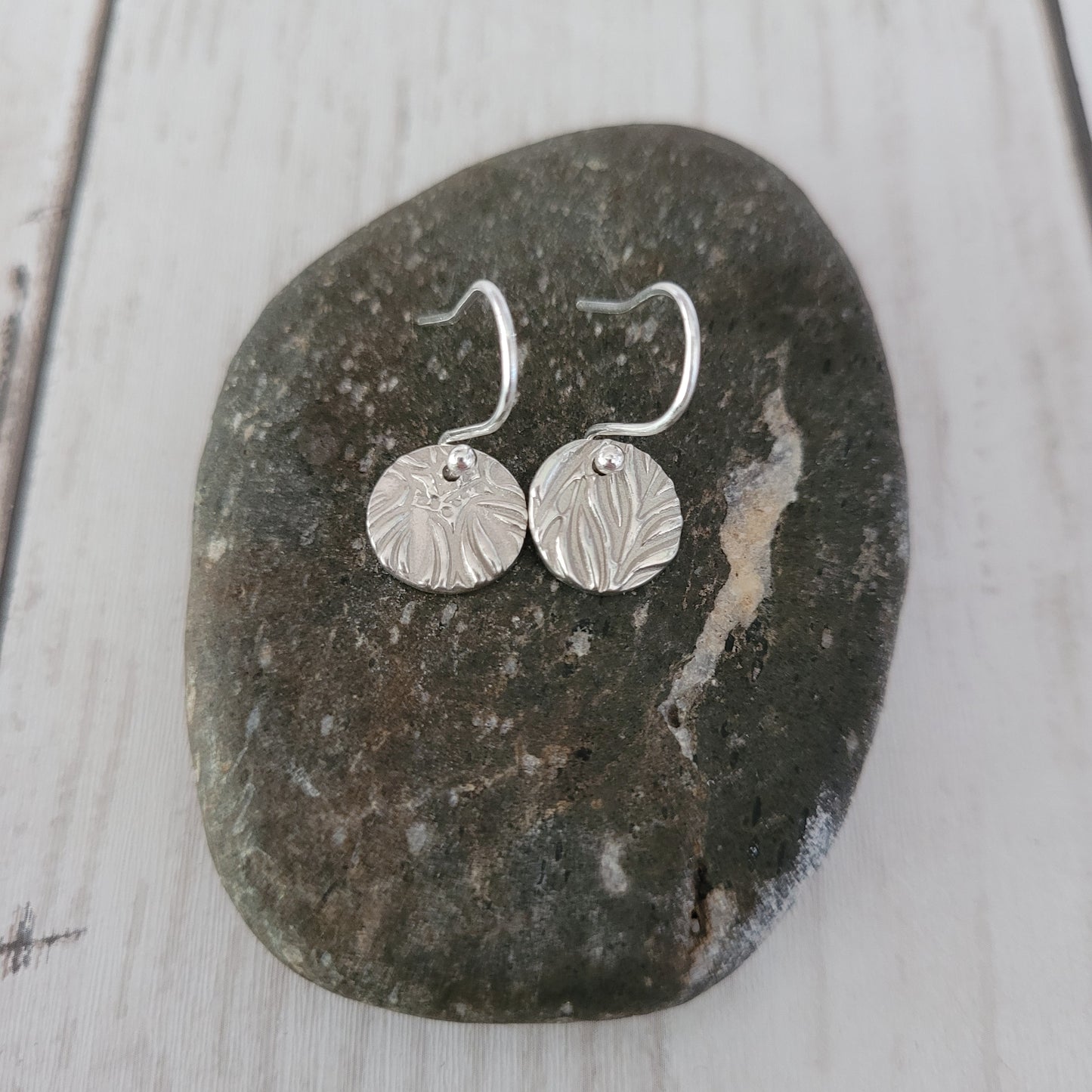 Silver round textured earrings on a dark stone surface