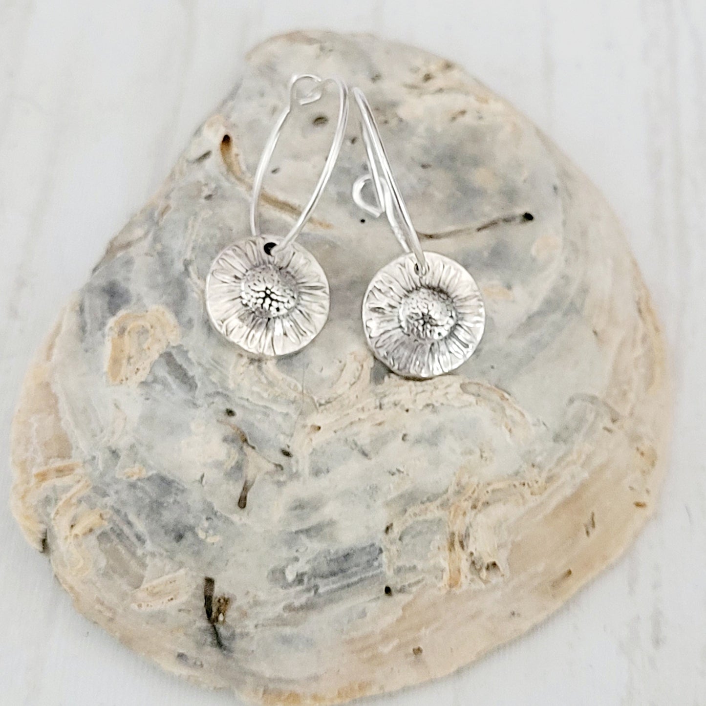 Silver hoop earrings on a textured shell surface with a white background