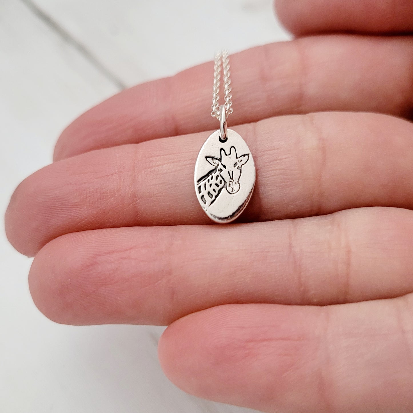 Silver necklace with a pendant shaped like a giraffe held between fingers on a white background
