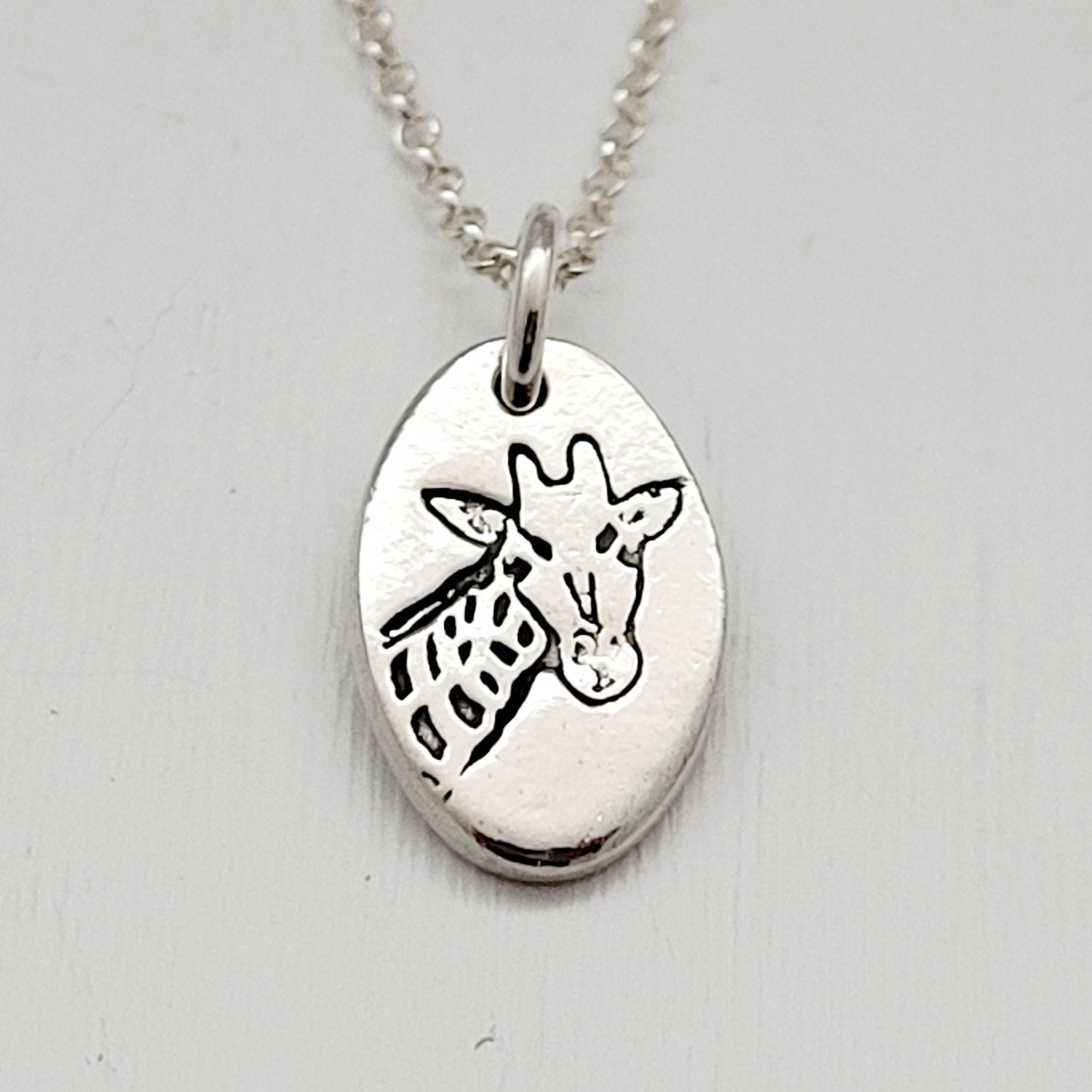 Silver pendant with a giraffe design on a light gray background