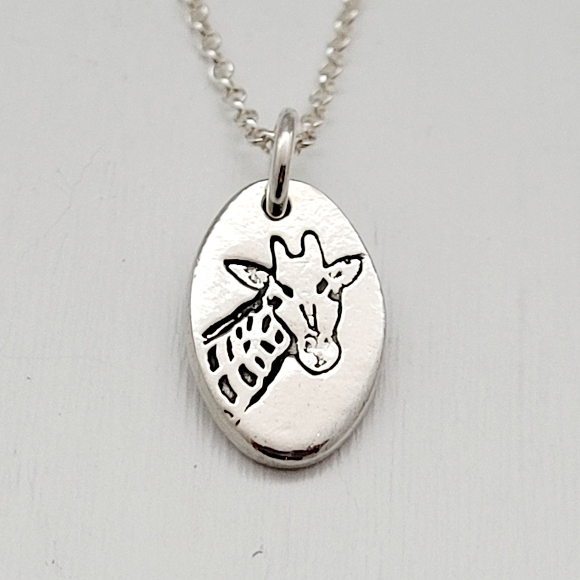 Silver pendant with a giraffe design on a light gray background