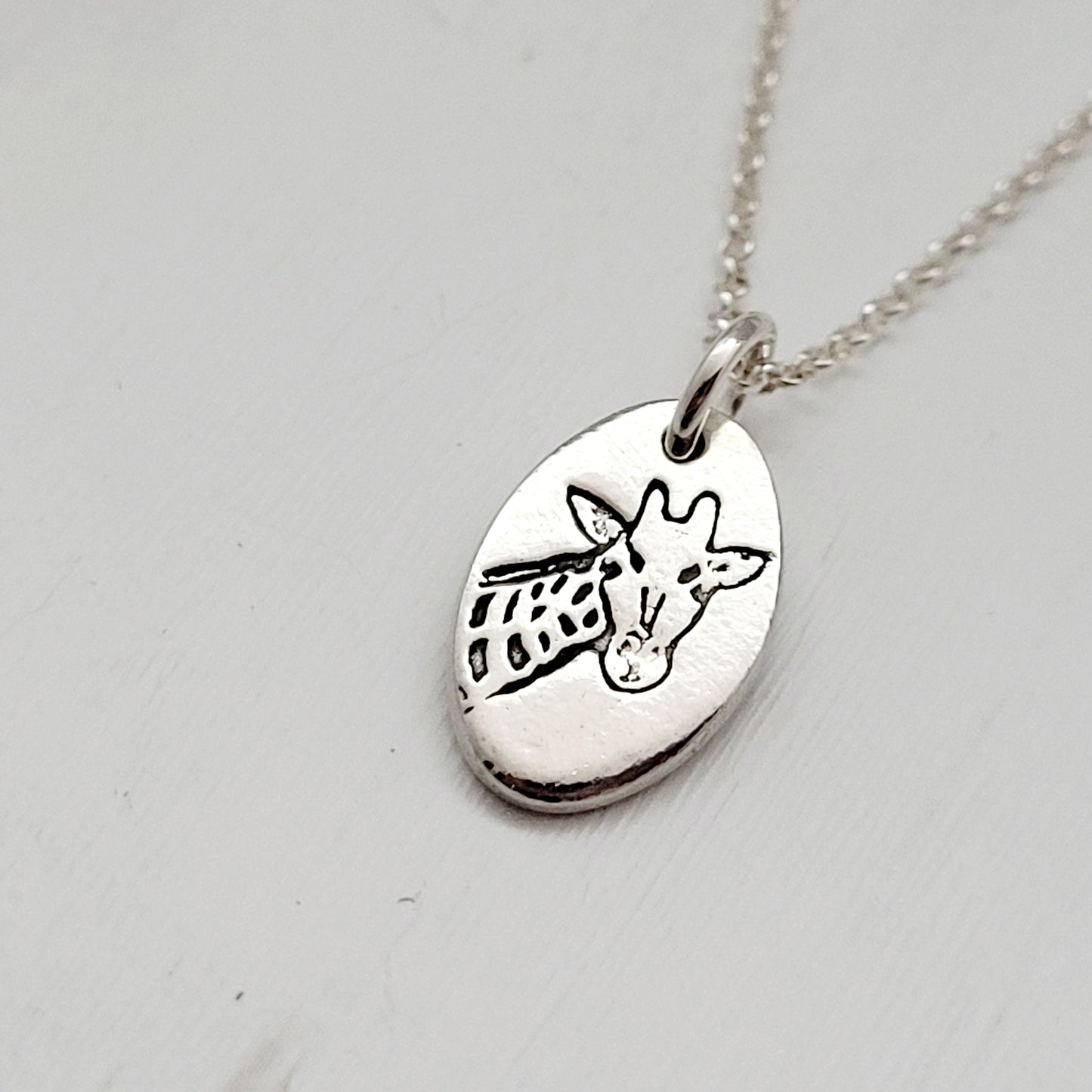 Silver necklace with a giraffe pendant on a light gray background